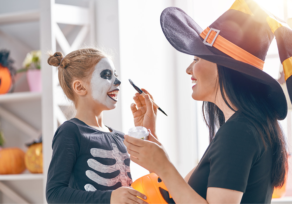 Woman face painting girl as a skeleton in their apartment home.