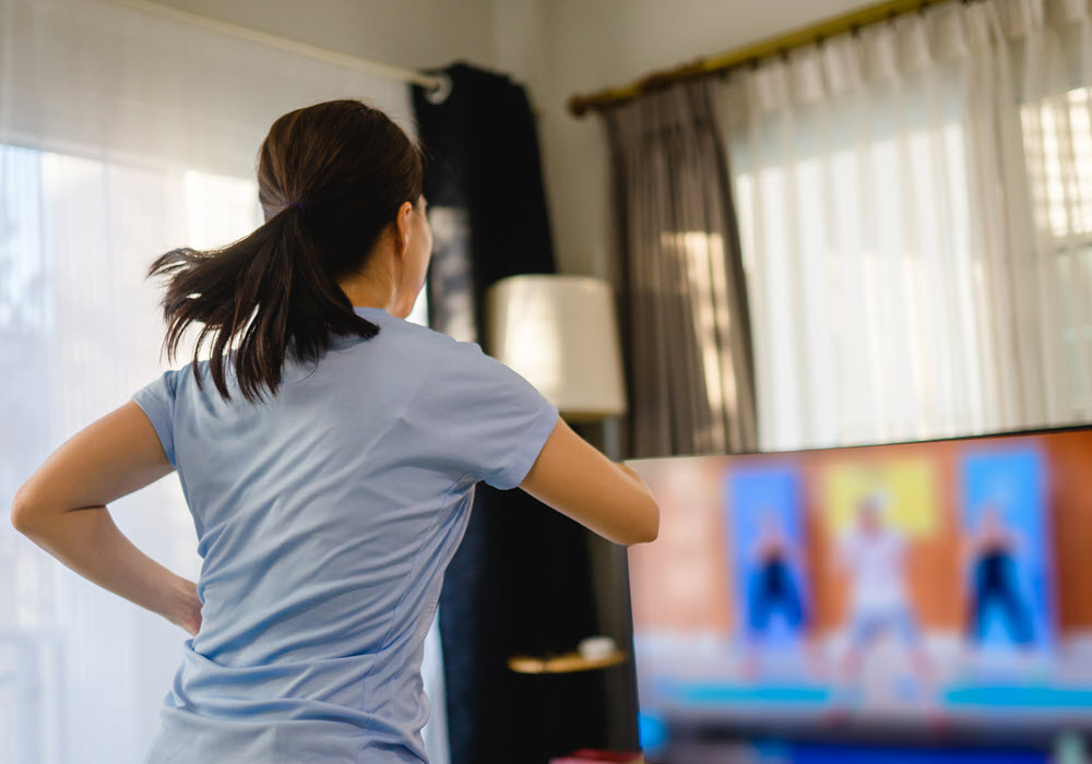 Woman following a workout routine on her television in apartment.