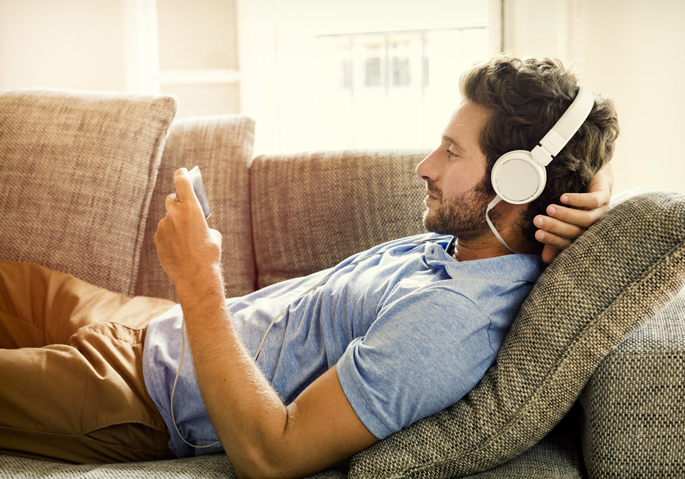 Man laying on sofa listening to music.