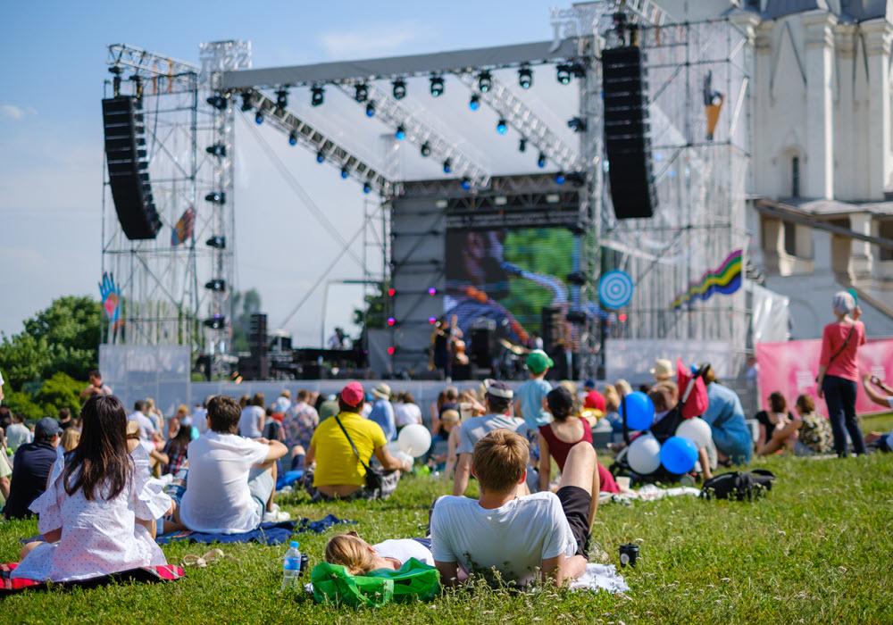 Festival go-ers sitting on grass listening to outdoor concert.