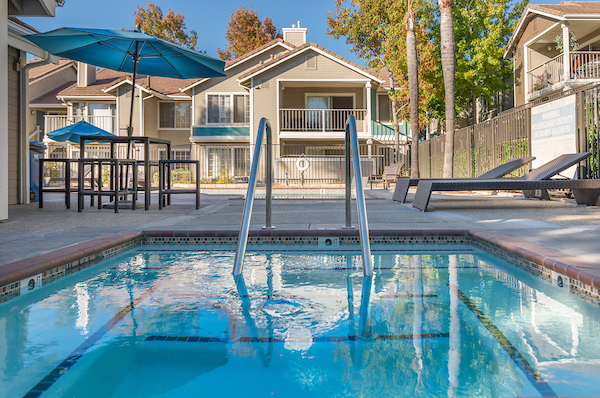 Outdoor swimming pool area with lounge seating and tables with umbrellas.