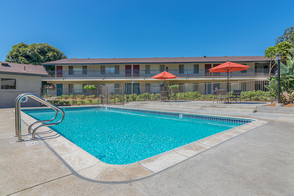 Outdoor swimming pool surrounded by tables, chairs, and umbrellas.